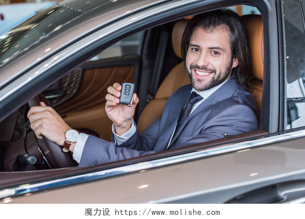 一个在汽车里全款买车的男人快乐的商人显示汽车钥匙, 而坐在新车在经销沙龙